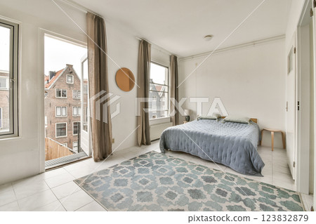 A beautifully designed modern bedroom featuring a large window, tasteful decor, and a cozy atmosphere, perfect for relaxation and comfort. 123832879