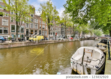 Picturesque canal scene in Amsterdam showcasing traditional buildings, trees, and parked boats along the water's edge. 123832920