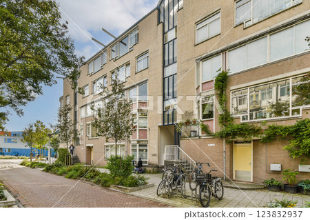 An urban residential building featuring a contemporary design with greenery and bicycles parked outside. The sidewalk offers a well-maintained atmosphere. 123832937