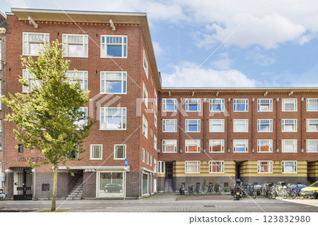 Showcasing contemporary urban buildings with red brick facades, large windows, and a tree, blending nature with architecture. 123832980