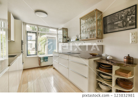 Bright and spacious kitchen showcasing sleek cabinetry and modern design, illuminated by abundant natural light through large windows. 123832981