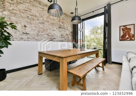 A chic dining area featuring a wooden table, bench seating, and an industrial aesthetic. The open windows allow natural light to enhance the rustic elements. A chic dining area featuring a wooden table, bench seating, and an industrial aesthetic. The open windows allow natural light to enhance the rustic elements. 123832996