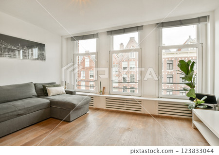 A stylish living room featuring a gray sectional sofa, natural light pouring in through large windows, and contemporary decor that enhances the space's openness. 123833044
