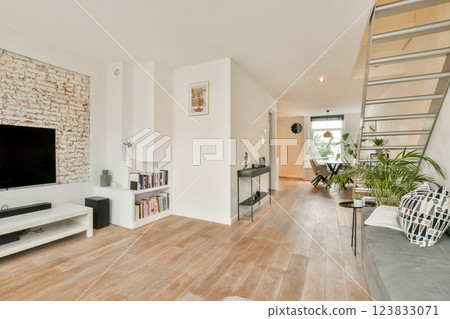 A stylish modern living room featuring light wood flooring, a decorative wall, and a cozy seating area adorned with plants and contemporary furniture. 123833071