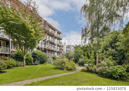 A serene garden pathway surrounded by greenery and modern apartments, creating a peaceful residential environment. 123833078