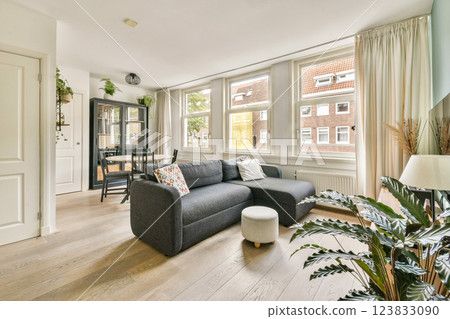 Cozy modern living room showcasing comfortable furniture, ample natural light through large windows, and a touch of greenery from indoor plants. 123833090