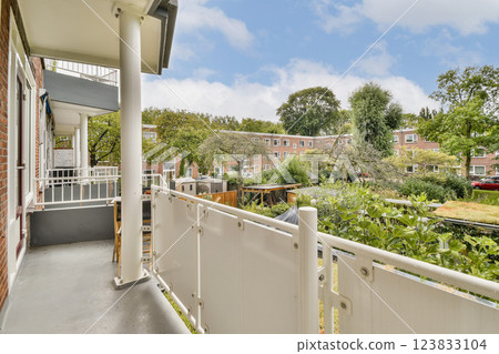 A serene balcony provides a picturesque view of a vibrant garden, surrounded by trees and residential buildings, making it a perfect spot for relaxation. 123833104