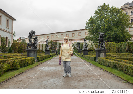 A female tourist walks around along a decorative alley decorated with many statues in a decorative park at Wallenstein Palace building in Prague in Czech Republic 123833144