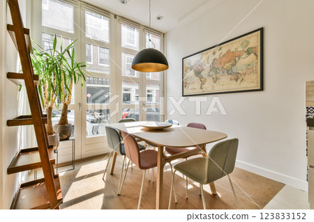 A bright dining space featuring a stylish wooden table surrounded by colorful chairs, illuminated by a pendant lamp, with a large world map on the wall. 123833152