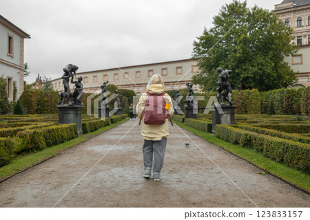 A female tourist walks around along a decorative alley decorated with many statues in a decorative park at Wallenstein Palace building in Prague in Czech Republic 123833157