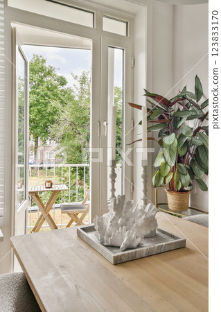 Bright and airy living space featuring an open balcony, a stylish dining setup, and lush green indoor plants enhancing the serene ambiance. 123833170