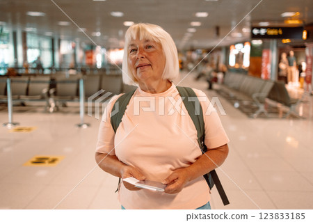 Happy blonde hair Elderly female tourist with a backpack with a passport while waiting for the passport check of the tourist at the airport Happy blonde hair Elderly female tourist with a backpack with a passport while waiting for the passport check of the tourist at the airport 123833185