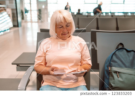 A cropped image of a beautiful Caucasian female tourist is holding her smartphone and passport, checking her flight information on her phone while sitting at a waiting seat in the airport terminal. A cropped image of a beautiful Caucasian female tourist is holding her smartphone and passport, checking her flight information on her phone while sitting at a waiting seat in the airport terminal. 123833203