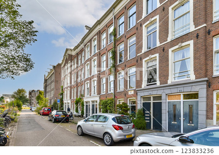 A picturesque street showcasing beautifully designed residential buildings surrounded by greenery and parked vehicles, offering a lively urban atmosphere. 123833236