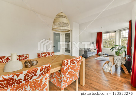 A stylish dining room with floral-patterned chairs, wooden flooring, and a warm ambiance created by natural light filtering through large windows. 123833276
