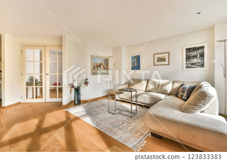 A stylish modern living room featuring a plush sofa, elegant artwork, and warm wooden flooring, creating a cozy ambiance for relaxation. 123833383