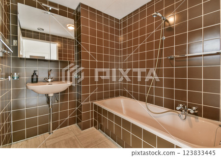 A stylish and contemporary bathroom featuring brown tiled walls, a sleek bathtub, and modern fixtures, emphasizing both aesthetics and functionality. 123833445