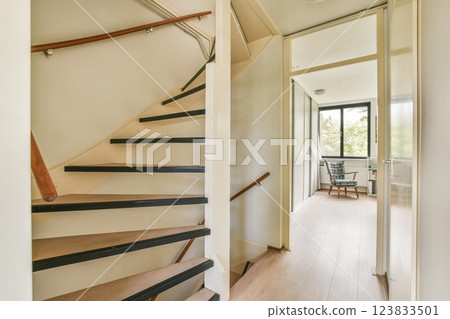 A sleek staircase leads to a well-lit hallway featuring contemporary design elements and a glimpse of a cozy living space beyond. 123833501