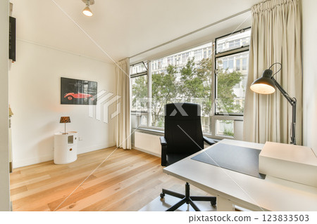 A contemporary workspace featuring a desk, chair, and large windows letting in natural light. Sleek design with minimalist decor enhances productivity. A contemporary workspace featuring a desk, chair, and large windows letting in natural light. Sleek design with minimalist decor enhances productivity. 123833503