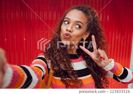 Fashion selfie, peace sign and happy woman against a red wall in city for fun travel holiday. Portrait urban girl show cool hand gesture and lips while traveling and sharing picture on social media Fashion selfie, peace sign and happy woman against a red wall in city for fun travel holiday. Portrait urban girl show cool hand gesture and lips while traveling and sharing picture on social media 123833528