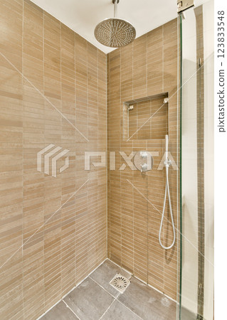 A sleek, contemporary shower space featuring textured beige tiles and a modern showerhead, creating a stylish and functional bathroom setting. 123833548