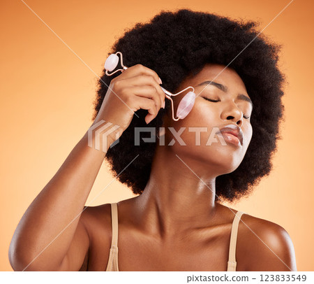 Beauty, afro and black woman with skincare derma roller for healthy and natural skin on face. Wellness and massage girl satisfied with rose quartz self care treatment with orange background. 123833549
