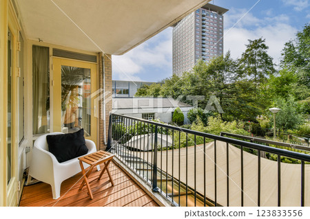 A bright urban balcony featuring a comfortable chair and chic wooden flooring, surrounded by lush greenery and modern architecture. A bright urban balcony featuring a comfortable chair and chic wooden flooring, surrounded by lush greenery and modern architecture. 123833556