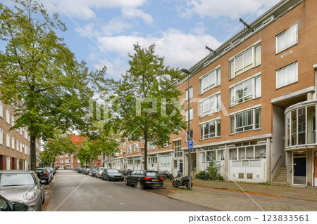 A serene urban street scene showcasing grey buildings, green trees, and parked cars, highlighting modern city life amid nature. 123833561