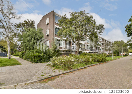 A contemporary apartment building set in a lush, green environment with trees and pathways, showcasing modern architecture and outdoor space. 123833600