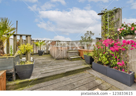 A tranquil rooftop garden featuring various plants and flowers, offering a perfect escape from the urban hustle. The wooden deck adds to the serene atmosphere. A tranquil rooftop garden featuring various plants and flowers, offering a perfect escape from the urban hustle. The wooden deck adds to the serene atmosphere. 123833615