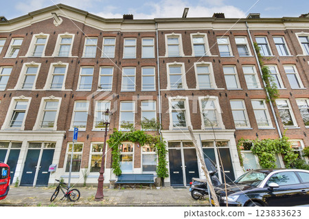 A picturesque brick building facade showcasing architectural details, large windows, and greenery adorning the entrance, set in a vibrant urban environment. 123833623