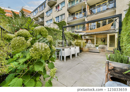 A tranquil urban garden featuring lush greenery and a modern patio seating area, perfect for relaxation and outdoor gatherings in a residential setting. 123833659