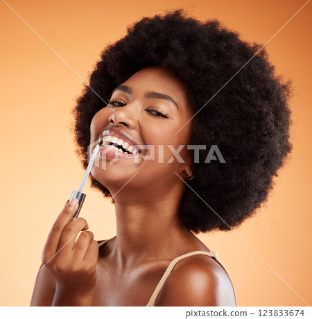 Lipgloss, smile and black woman excited about makeup against an orange studio background. Face portrait of a young African girl model with lipstick and cosmetic beauty product for care of lips 123833674