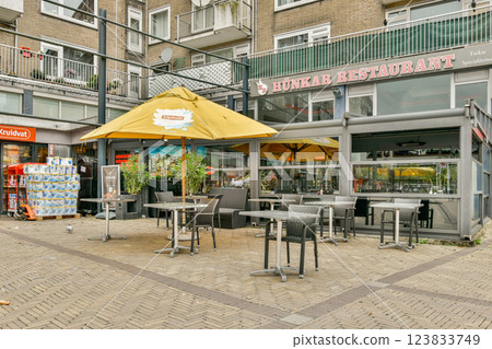 An inviting outdoor restaurant features tables under yellow umbrellas, surrounded by urban scenery, creating a warm dining atmosphere for guests. An inviting outdoor restaurant features tables under yellow umbrellas, surrounded by urban scenery, creating a warm dining atmosphere for guests. 123833749
