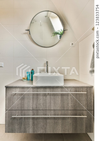 Sleek and stylish bathroom featuring a wooden vanity, a round mirror, and modern fixtures that create a serene atmosphere. Sleek and stylish bathroom featuring a wooden vanity, a round mirror, and modern fixtures that create a serene atmosphere. 123833754