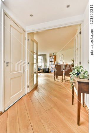 A spacious modern interior showcasing natural wood flooring and an open doorway that leads to a well-lit living area adorned with furniture and plants. 123833811