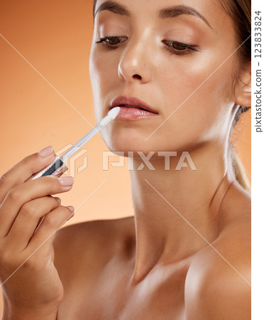 Beauty, makeup and lip gloss with woman in a studio for grooming, hygiene and lips cosmetics. Face, skincare and model apply lipstick against a brown background for full, feminine and natural lip Beauty, makeup and lip gloss with woman in a studio for grooming, hygiene and lips cosmetics. Face, skincare and model apply lipstick against a brown background for full, feminine and natural lip 123833824