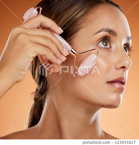 Woman, beauty and skincare rolling tool for natural wellness massage mockup on an orange studio background. Clean, facial health and cosmetic wellbeing during skin self care anti aging routine at spa 123833827