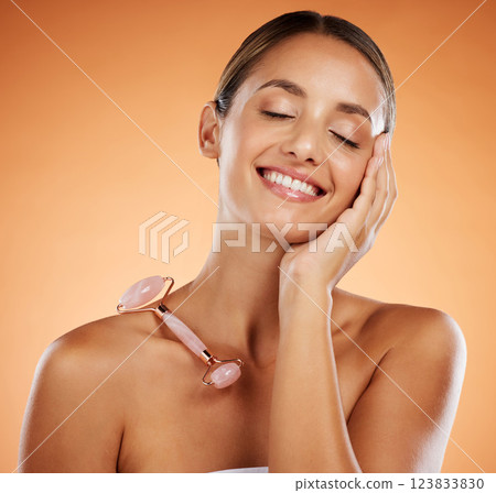 Happy woman in studio, skincare stone roller tool for facial massage and luxury cosmetic product. Pink rose quartz gua sha, smooth soft face and young natural beauty in wellness treatment in studio 123833830