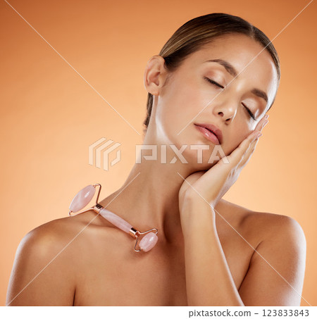 Skincare, beauty and face roller massage with woman in studio background for grooming, hygiene and wellness. Facial, dermatology and wrinkle prevention with model enjoying stone roller tool 123833843