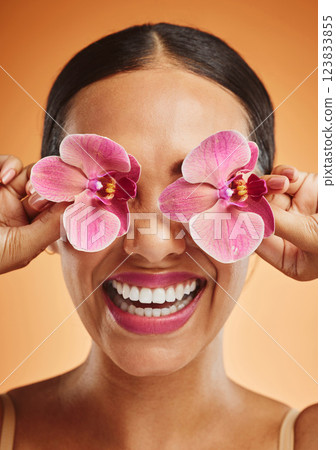 Orchid flower, creative art and beauty woman with makeup, cosmetic and smile on face against an orange background. Happy, floral and comic female model with plant for facial wellness and skincare 123833855