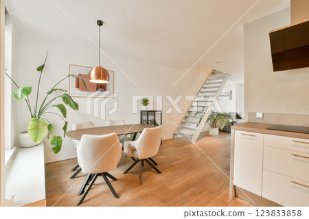 A contemporary living space featuring a well-lit room with stylish furniture, indoor plants, and a staircase, exuding comfort and elegance. 123833858
