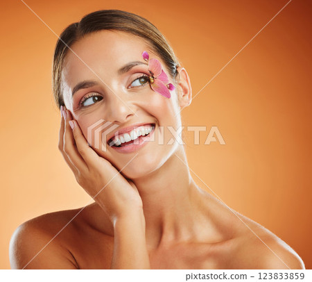 Model, flower and eye with makeup in studio with smile for fashion, cosmetics or beauty against backdrop. Woman, orchid and floral art for eyes with skincare, happy and face orange background 123833859