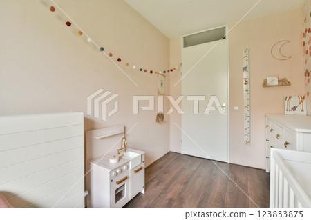 A beautifully designed nursery room featuring soft pastel colors, a stylish crib, playful decorations, and a warm wooden floor, creating a perfect space for a baby. 123833875