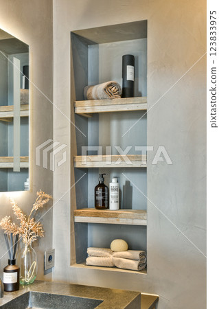 Aesthetic display of towels and toiletries on wooden shelves in a minimalist bathroom setting, complemented by natural decor elements. Aesthetic display of towels and toiletries on wooden shelves in a minimalist bathroom setting, complemented by natural decor elements. 123833975