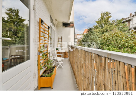 A cozy balcony featuring a wooden fence, potted plants, and comfortable seating, surrounded by lush greenery and a bright sky overhead. 123833991
