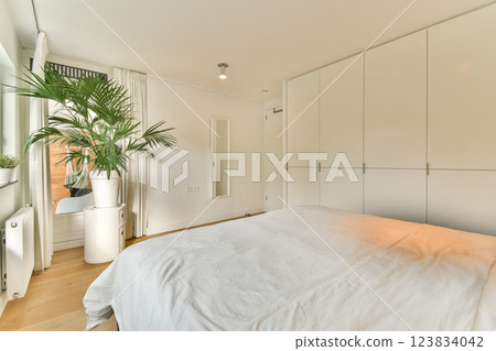 A serene modern bedroom featuring a light color palette, a large plant, and minimalist furniture. The space exudes calm and simplicity, perfect for relaxation. A serene modern bedroom featuring a light color palette, a large plant, and minimalist furniture. The space exudes calm and simplicity, perfect for relaxation. 123834042