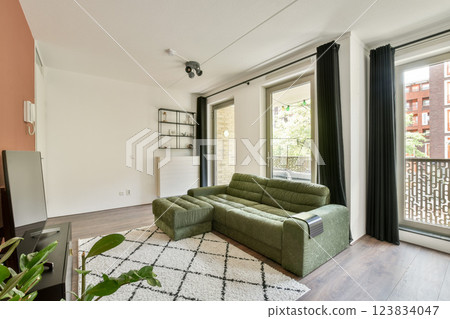 A contemporary living room featuring a green sofa, large windows, and a modern aesthetic, providing a bright and inviting atmosphere for relaxation. A contemporary living room featuring a green sofa, large windows, and a modern aesthetic, providing a bright and inviting atmosphere for relaxation. 123834047
