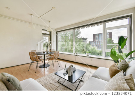 A stylish modern living room featuring a cozy seating area, a chic coffee table, and large windows offering a view of city greenery. Perfect for relaxation and socializing. 123834071
