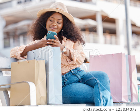 Phone, shopping and happy black woman with shop and store bags on a bench outdoor. Online, mobile and ecommerce app scroll of a young person smile from Miami with technology and retail paper bag 123834072